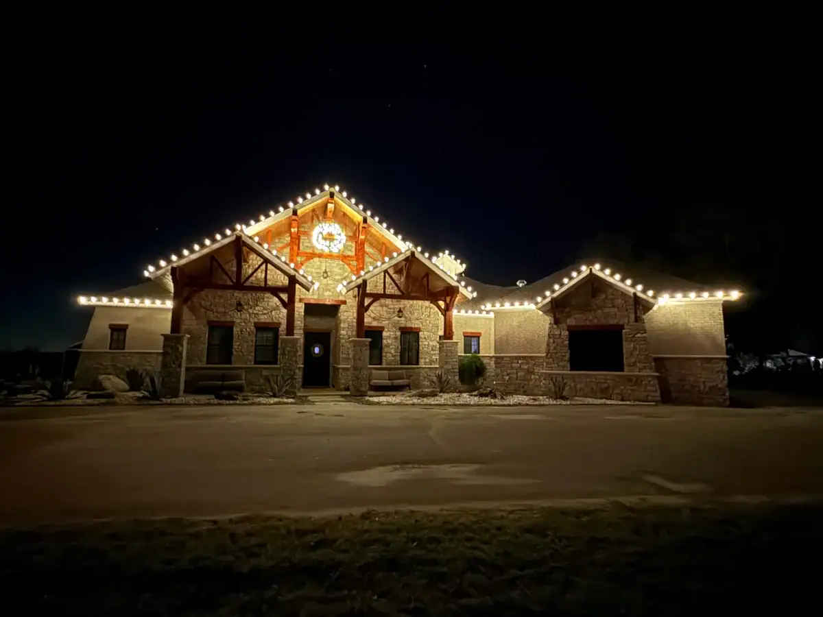 Christmas lights tracing a home’s roofline with a wreath above the entrance